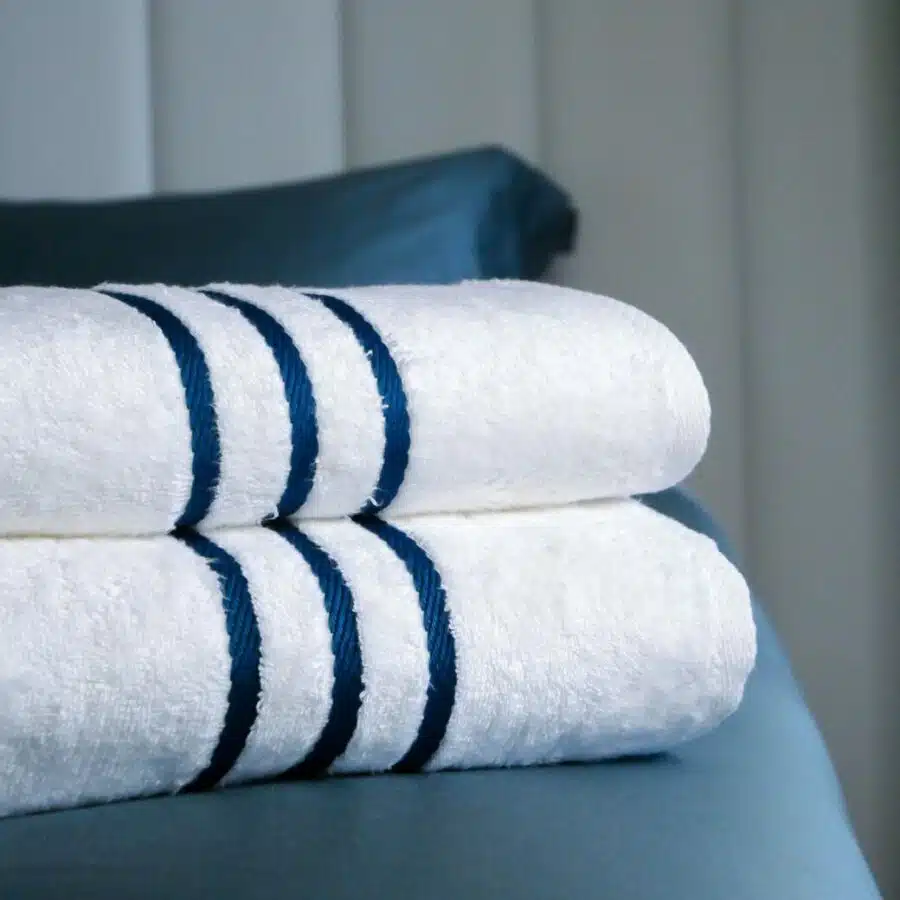 Serviettes en tissu de bambou soigneusement pliées et déposées avec soin sur le lit d'une suite d'hôtel, soulignant l'attention portée aux détails pour offrir un confort exceptionnel