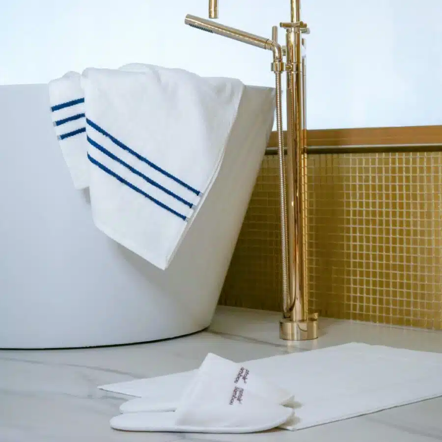 Serviette en bambou douce et absorbante joliment pliée et placée sur le rebord d'une baignoire haut de gamme, complétant l'atmosphère de luxe de cette salle de bain design. Des chaussons de bain d'une qualité incroyable complète ce joli assortiment de bain