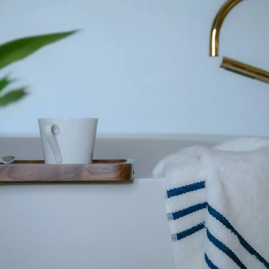 Image d'une serviette en bambou douce et moelleuse placée avec soin sur le rebord d'une baignoire, aux côtés d'un élégant plateau et d'une tasse de café, offrant un moment de détente luxueux.