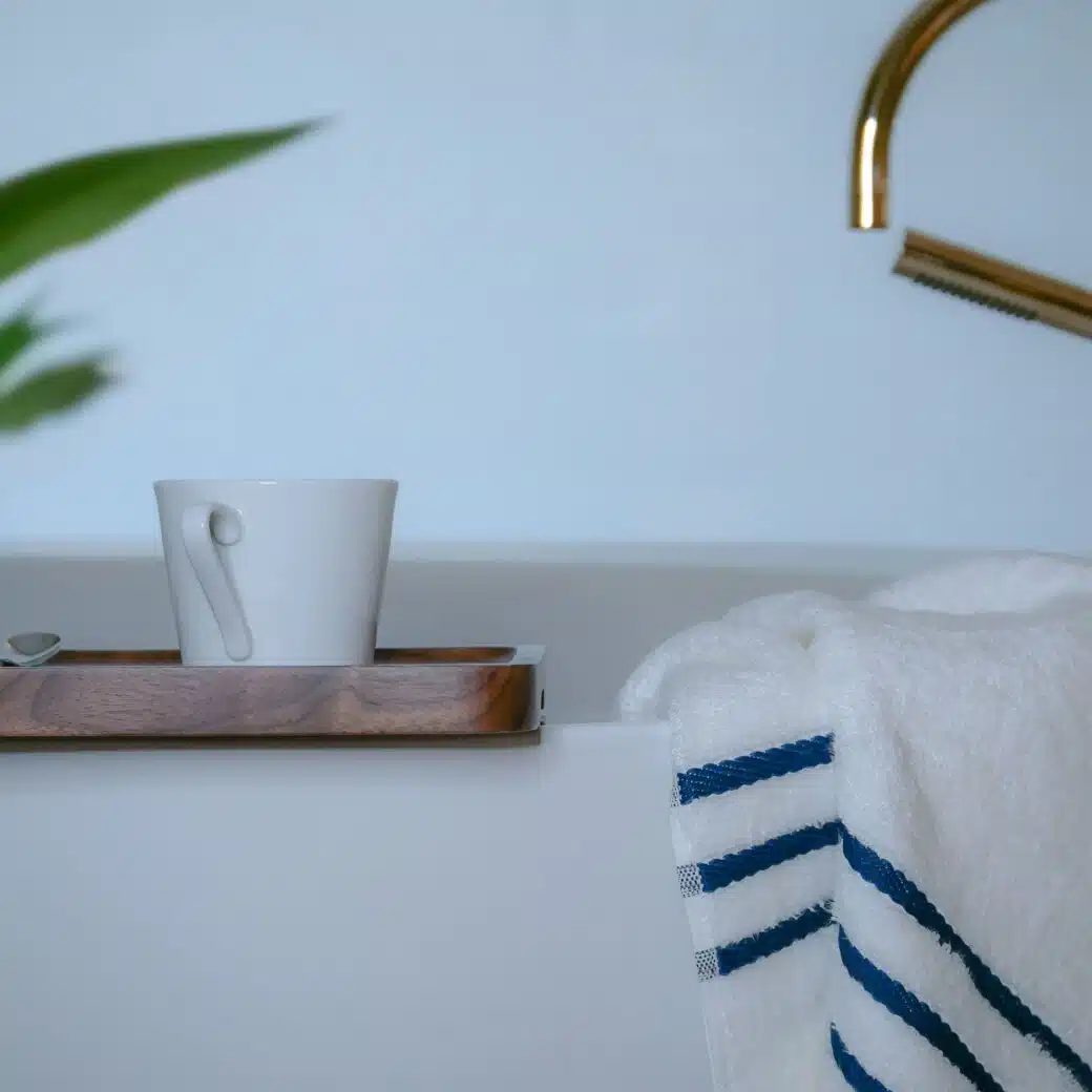 Image d'une serviette en bambou douce et moelleuse placée avec soin sur le rebord d'une baignoire, aux côtés d'un élégant plateau et d'une tasse de café, offrant un moment de détente luxueux.