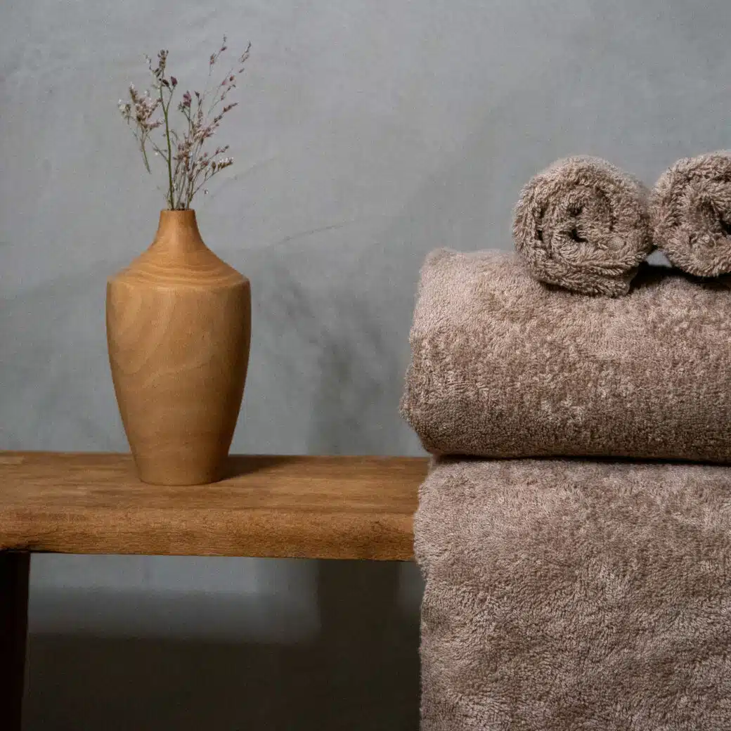 Dans une salle de bain luxueuse, une serviette en pulpe de bois et fibre de bambou repose délicatement sur un banc en bois, créant une atmosphère de sérénité et d'élégance. Sa texture douce et sa couleur naturelle s'harmonisent parfaitement avec l'environnement, offrant une expérience de confort suprême tout en incarnant un engagement envers la durabilité et l'écologie. Un ajout raffiné à cet espace dédié au bien-être et à la relaxation.