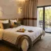 Chambre d’hôtel haut de gamme au style chaleureux, avec un lit en linge blanc légèrement texturé, un plateau de petit-déjeuner, lumière naturelle douce et décoration élégante donnant sur une terrasse arborée.
